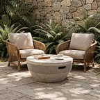 A textured concrete coffee table paired with woven rattan chairs in a lush garden courtyard. Offering a striking material contrast for boutique hotel exterior styling.